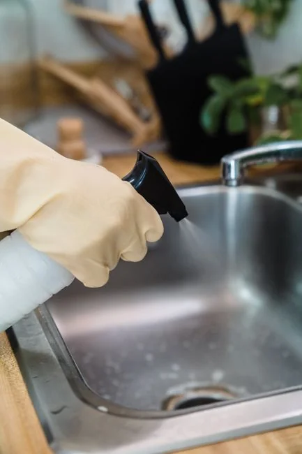 Recadrage d’un homme sans visage portant des gants en caoutchouc orange, nettoyant la buse de la douche avec une éponge